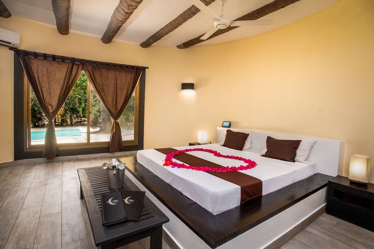 Habitación de hotel con cama, mesita de noche, lámpara y vista a una piscina.