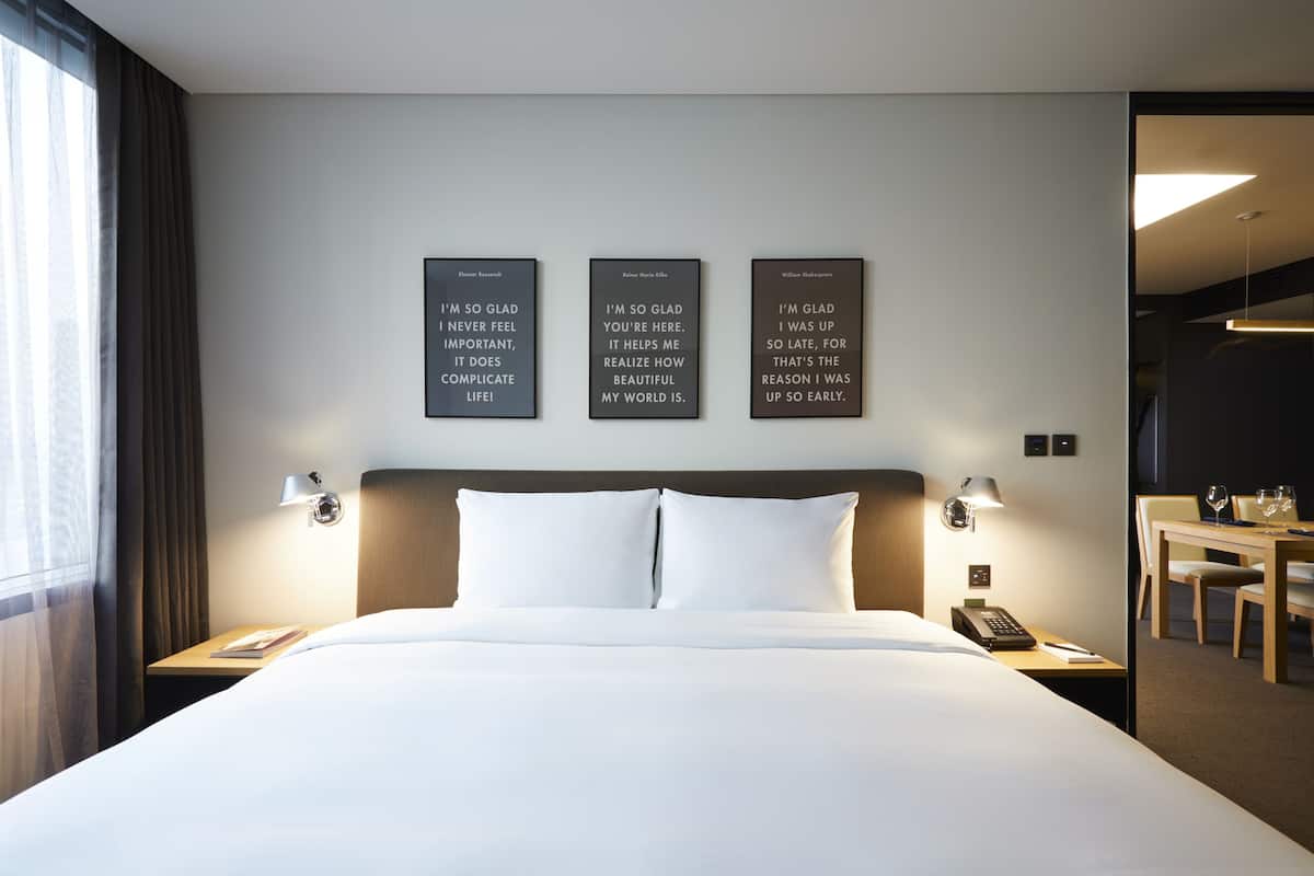 A hotel room with a large bed, two bedside tables with lamps, a desk with a chair, and three framed quotes on the wall.