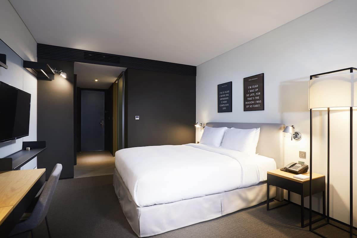 A modern hotel room with a large bed, a desk, a flat-screen TV, and a bedside lamp.