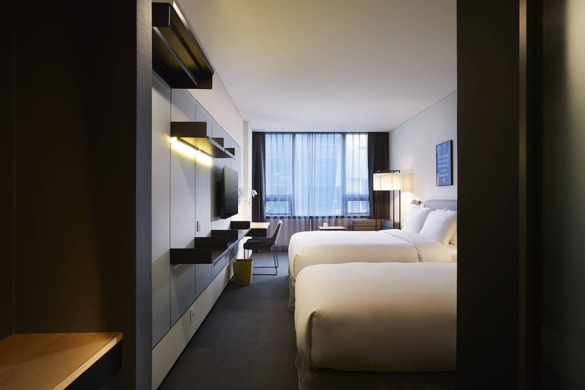 A hotel room with a bed, a desk, a chair, a TV, and a window with curtains.