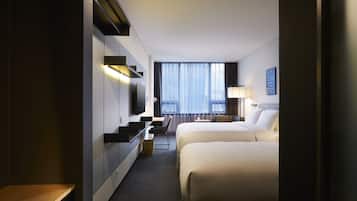 A hotel room with a bed, a desk, a chair, a TV, and a window with curtains.
