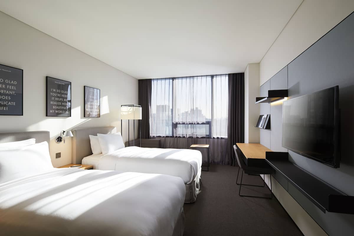 A hotel room with two beds, a desk, a TV, and a window with curtains.