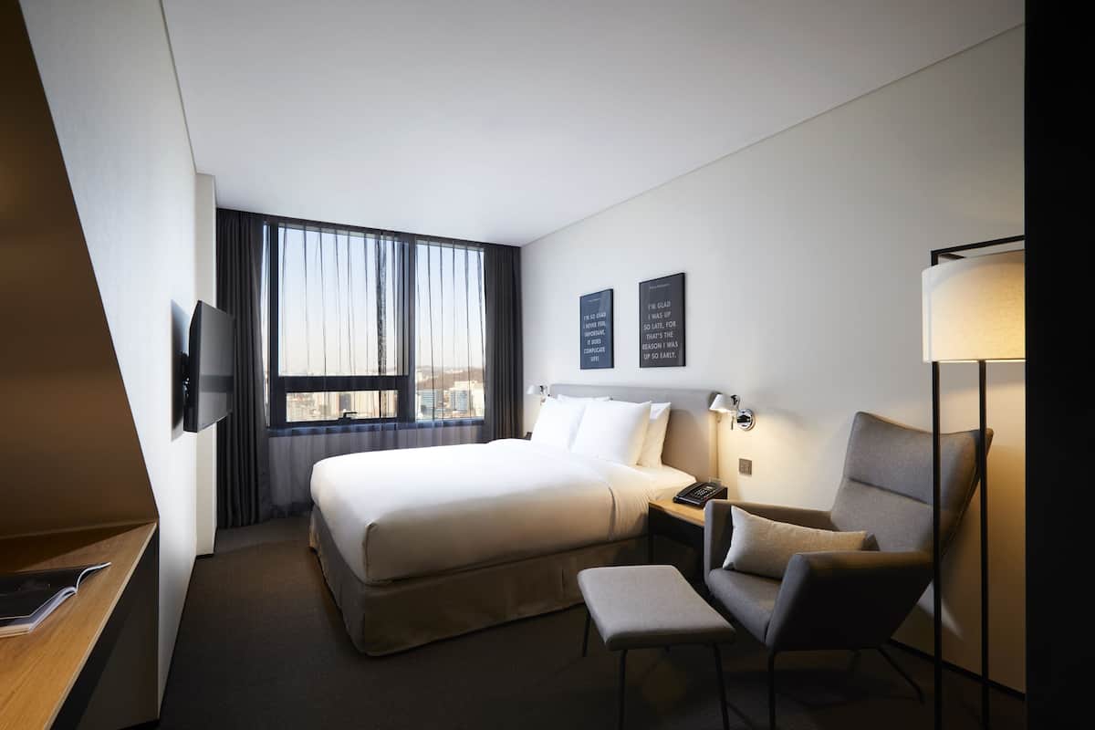 A hotel room with a large bed, a desk, a chair, a TV, and a window with curtains.