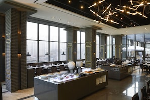 A modern restaurant with a buffet setup, large windows, and a city view.