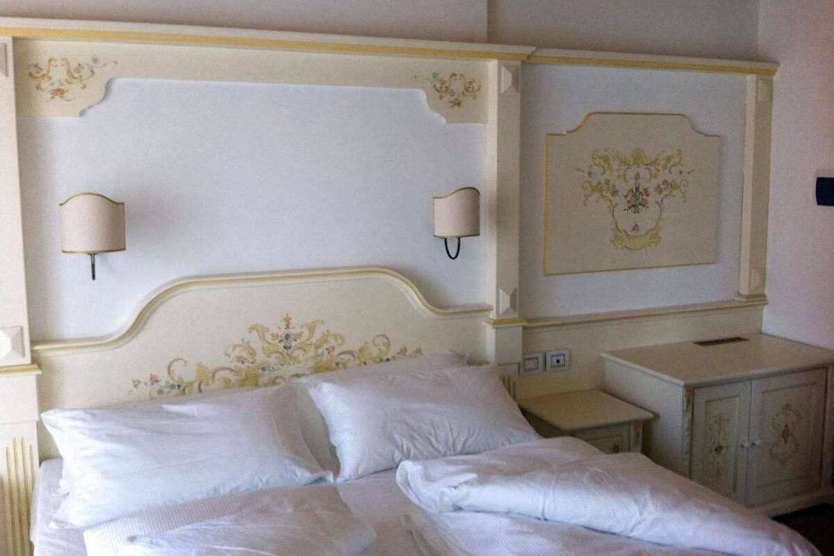 Una cama bien tendida con sábanas blancas, un cabecero decorativo y lámparas de pared.