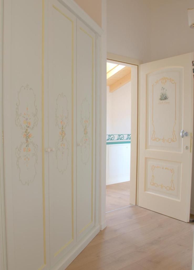 Un couloir au plancher de bois mène à une pièce dont la porte blanche est ornée de motifs floraux et d’un petit emblème.