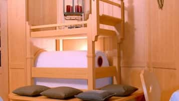 Una cama individual con cabecera de madera, una mesita con lámpara y un crucifijo colgado en la pared.