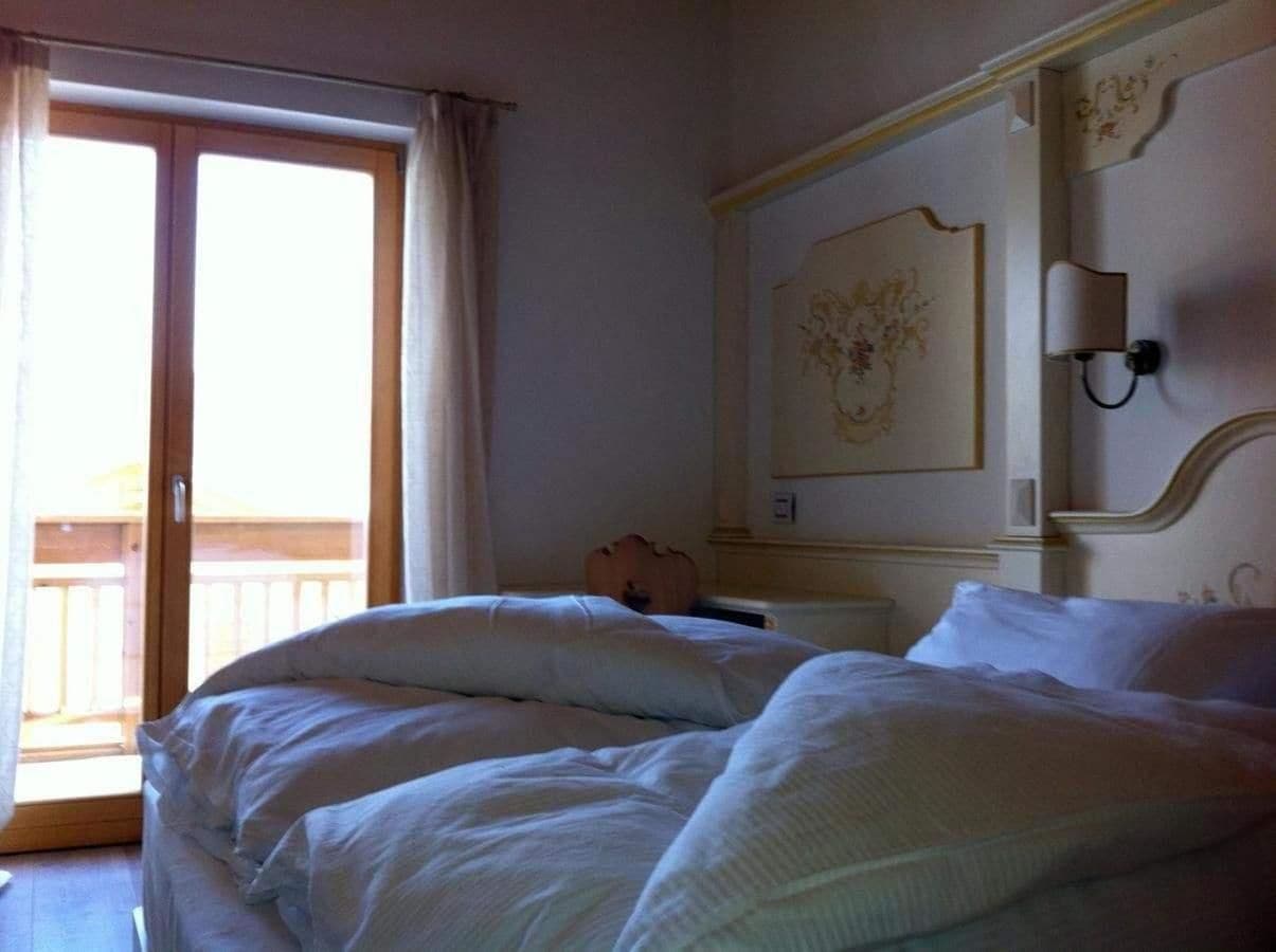 Habitación de hotel con una cama grande, un balcón y un adornado cabecero.