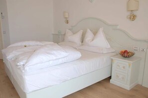 A neatly made bed with white linens and pillows, a bedside table with a fruit bowl, and a wall-mounted lamp. - Relais Fior di Bosco (Folgaria)