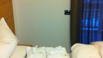 A hotel room with a neatly made bed, a heart-shaped light fixture on the wall, and a window with curtains.