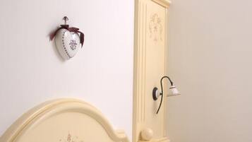 A bed with white linens, a decorative headboard, a wall-mounted light fixture, and a small bedside table with a fruit bowl.