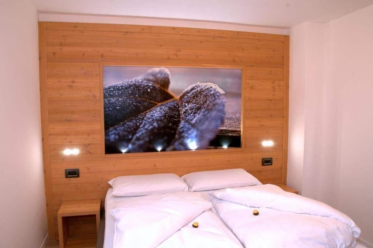 Un dormitorio con una cama grande, un panel de pared de madera y un televisor montado que muestra un paisaje nevado.