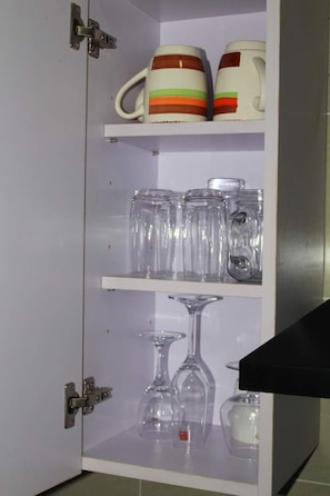 A cabinet with shelves containing mugs, glasses, and a wine glass.