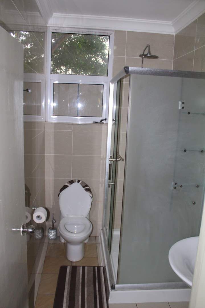 A bathroom with a toilet, a glass-enclosed shower, and a window above the toilet.