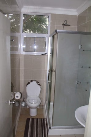 A bathroom with a toilet, a glass-enclosed shower, and a window above the toilet.