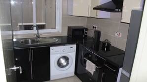 A compact kitchen with a washing machine, a microwave, and a stove. - James East Legon Piece (Accra)