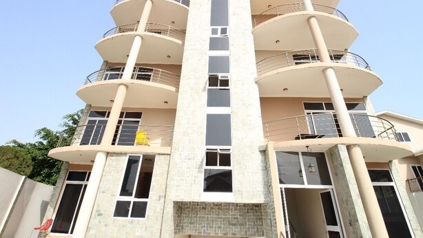 A multi-story building with balconies on each floor, large windows, and a central vertical feature. - James East Legon Piece (Accra)