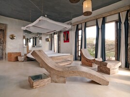 Una habitación con una cama grande, un sillón de madera, una mesita pequeña y un dosel colgante.