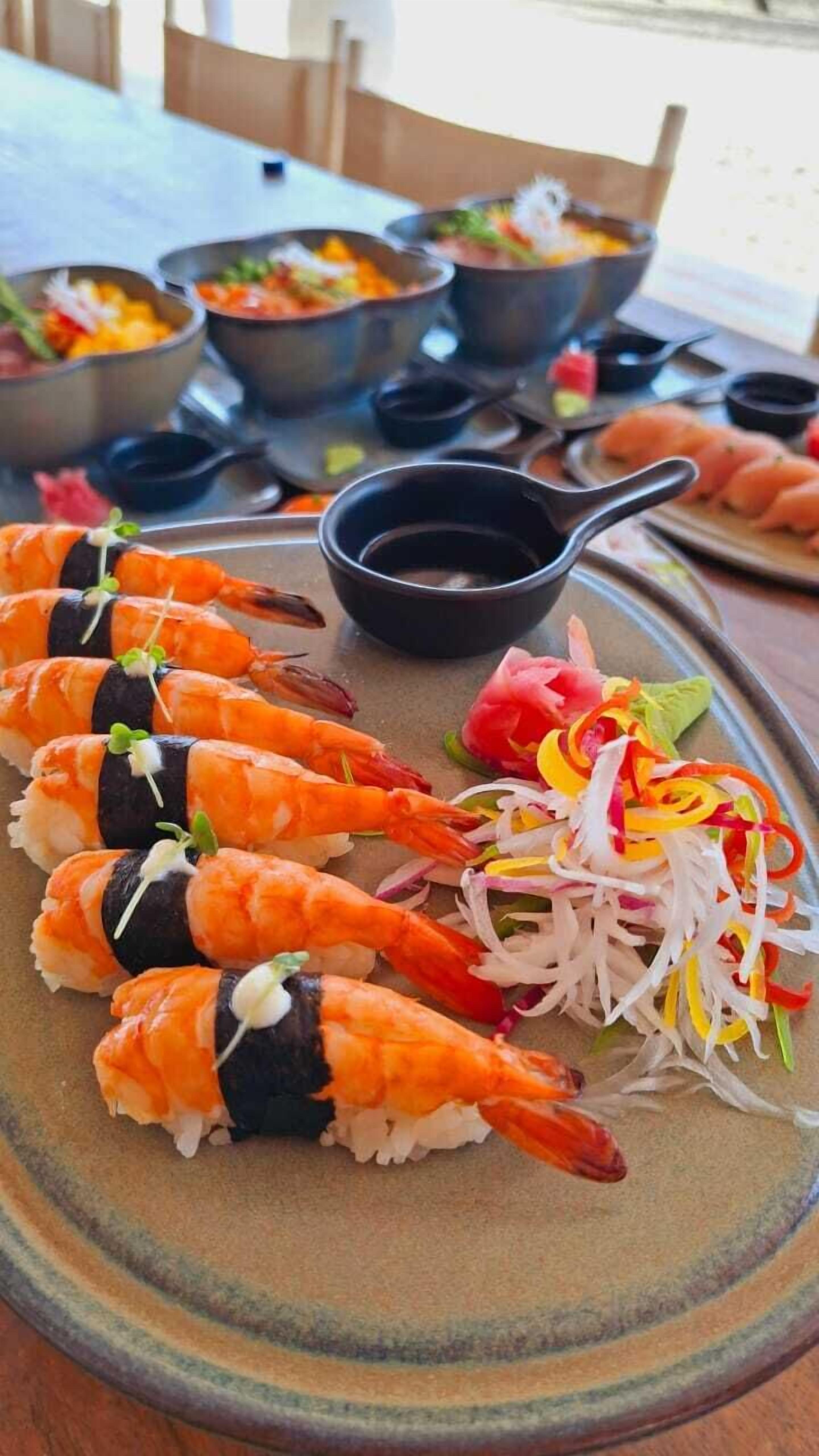 A plate of sushi with shrimp, a bowl of dipping sauce, and a side of pickled vegetables.