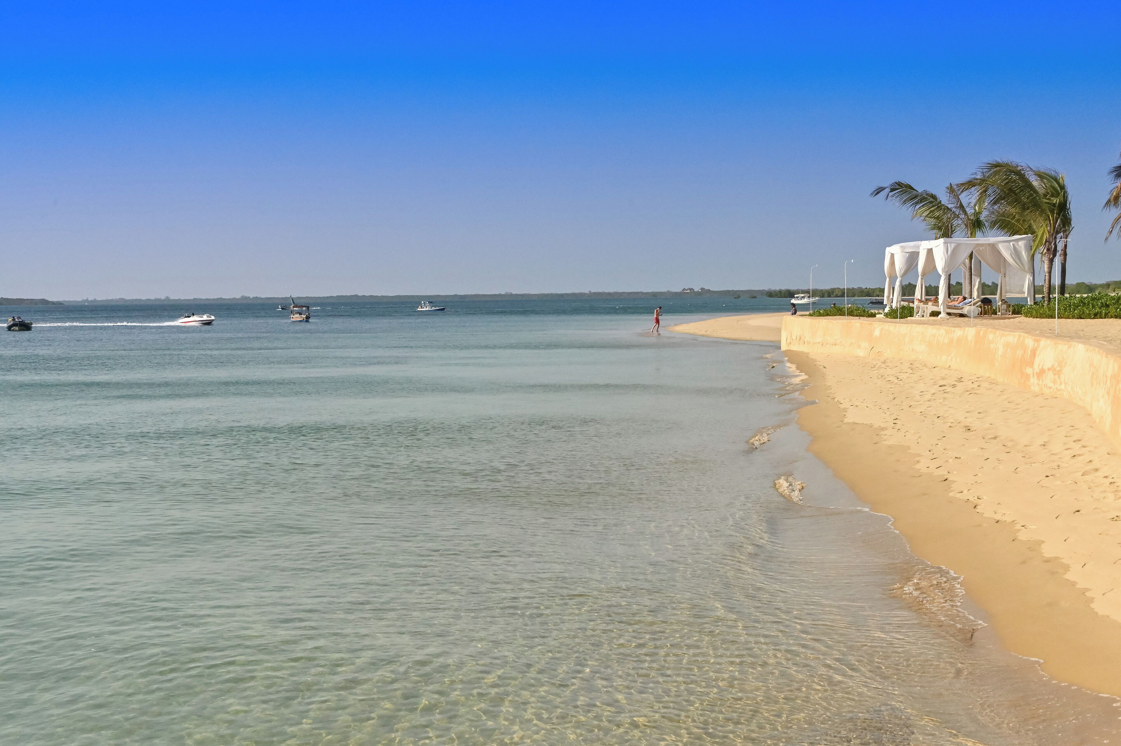 Una playa con agua cristalina, un quiosco blanco y palmeras.