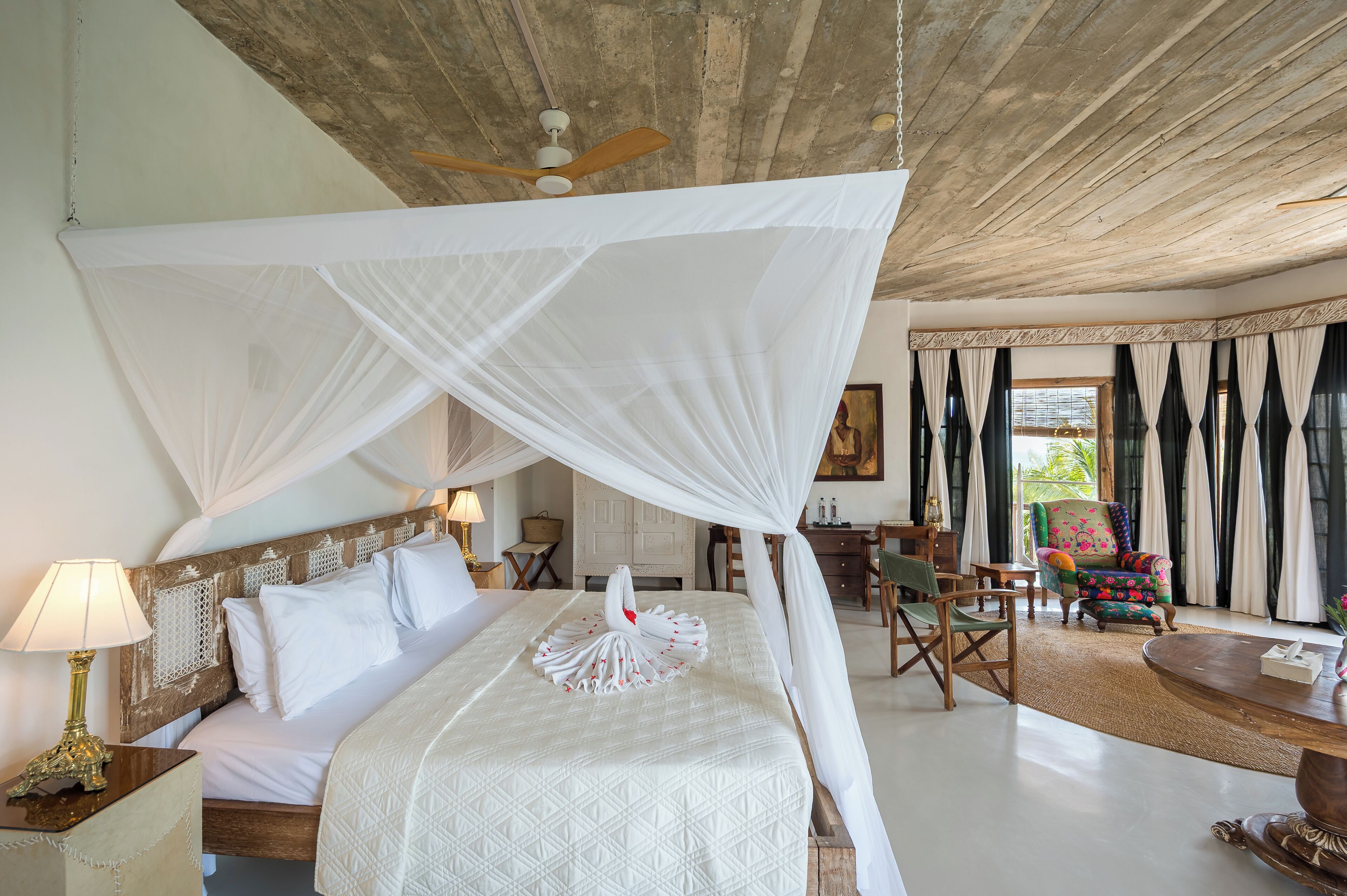 Een slaapkamer met een hemelbed, een plafondventilator en uitzicht op de omgeving.