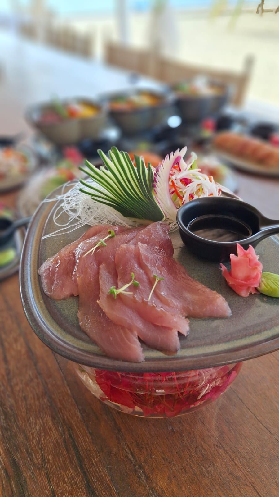 A plate of sashimi with a decorative garnish, a small bowl of soy sauce, and a wooden table.