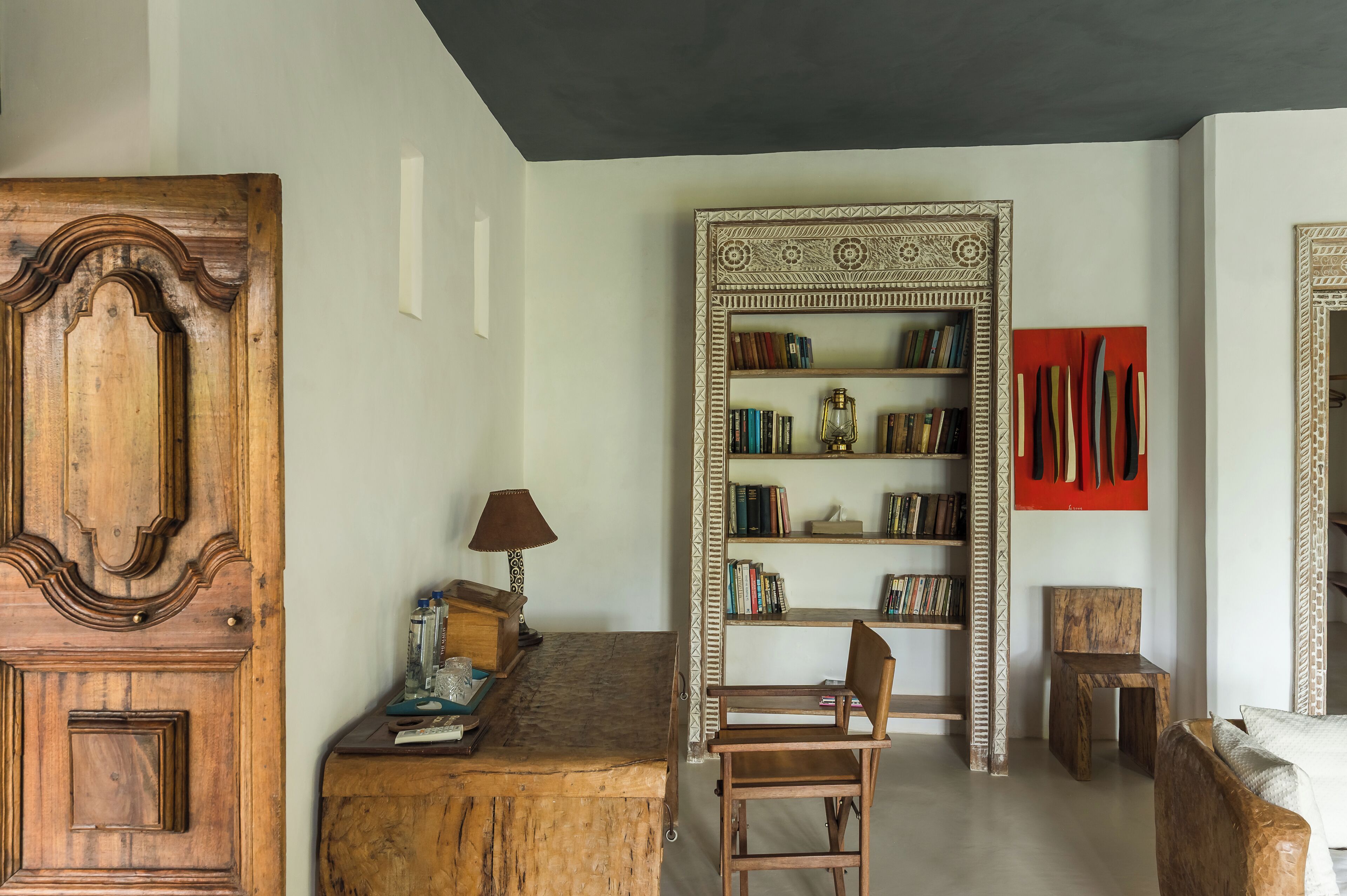 A room with a wooden cabinet, a desk with a lamp, a bookshelf, and a chair.