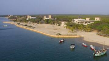 An aerial view of a coastal area with several boats anchored near the shore, a sandy beach, and buildings with a tropical setting.