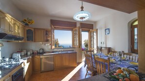 A spacious kitchen with wooden cabinets, a stainless steel dishwasher, and a dining area with a table set for four. - Elegant & Panoramic Villa with Sea View Solarium (Furore)