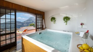 A spa room with a hot tub, a balcony with a view of mountains, and a small shelf with a plant and a vase. - Elegant & Panoramic Villa with Sea View Solarium (Furore)