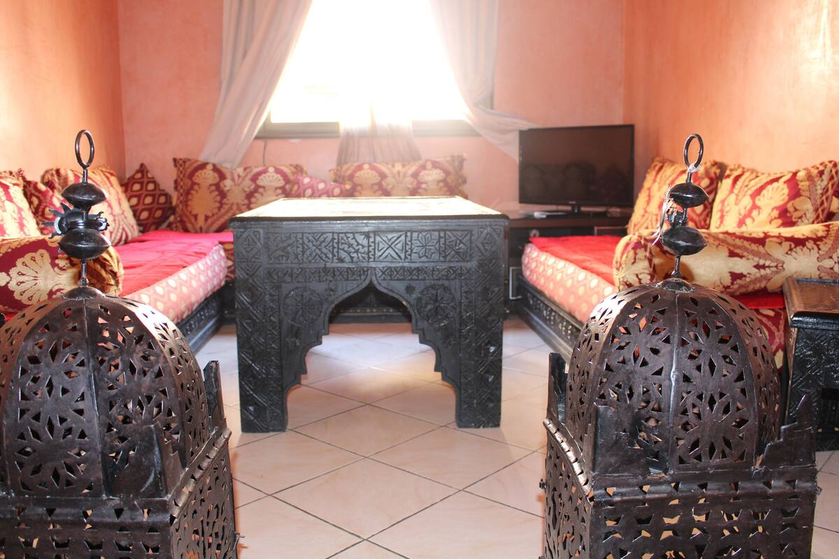 A traditional Moroccan room with a patterned sofa, a low table, and ornate chairs.