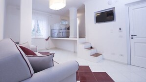 Una sala de estar moderna con un sofá, una escalera, un televisor montado en la pared y una puerta.