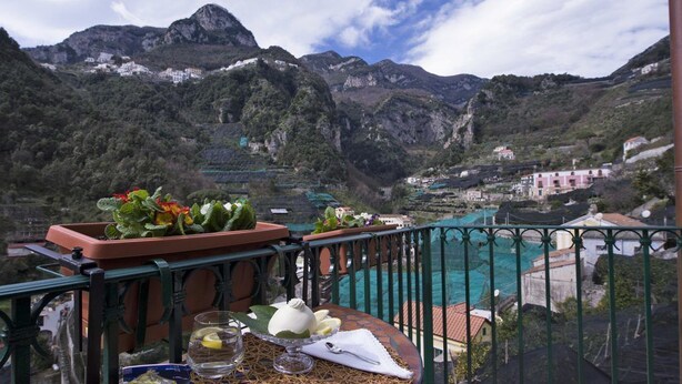 Un balcón con vistas a un paisaje montañoso, una piscina y una mesa con un florero y un vaso de agua.