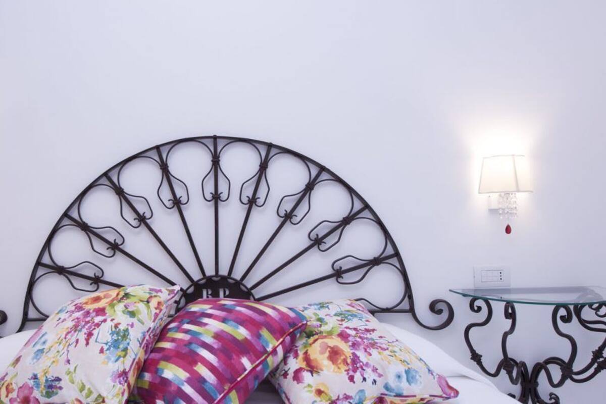 Una cama con cabecera metálica, dos mesitas de noche y dos lámparas de pared.