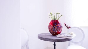 Una mesa redonda con un florero rojo que contiene flores blancas, un libro y una pequeña flor blanca encima.