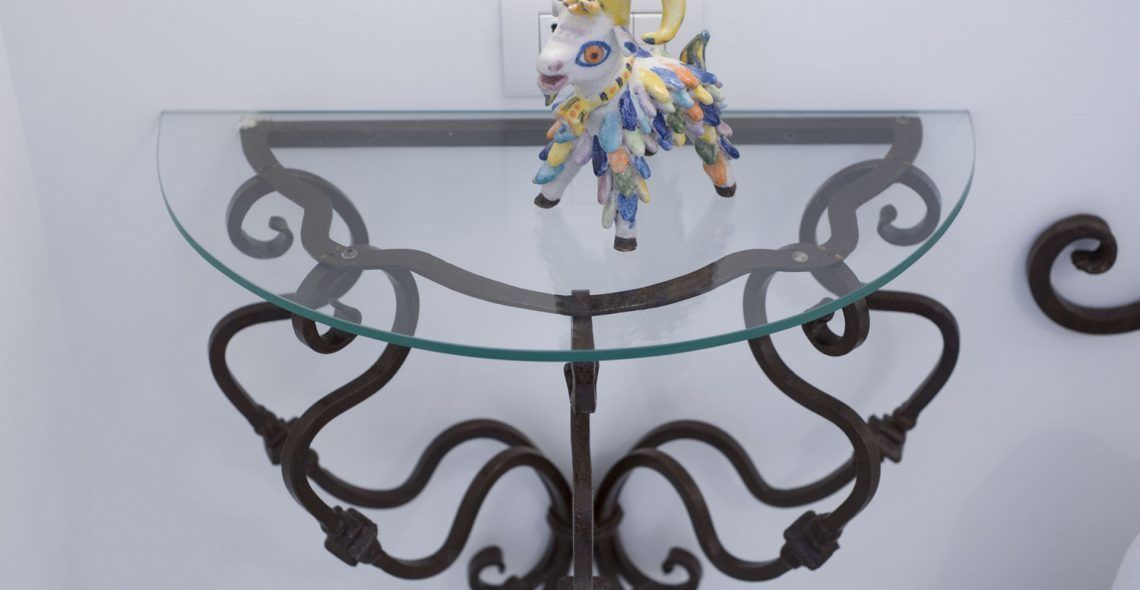 Ein Tisch mit Glasplatte, verzierten Metallbeinen und einer dekorativen Pferdefigur darauf.