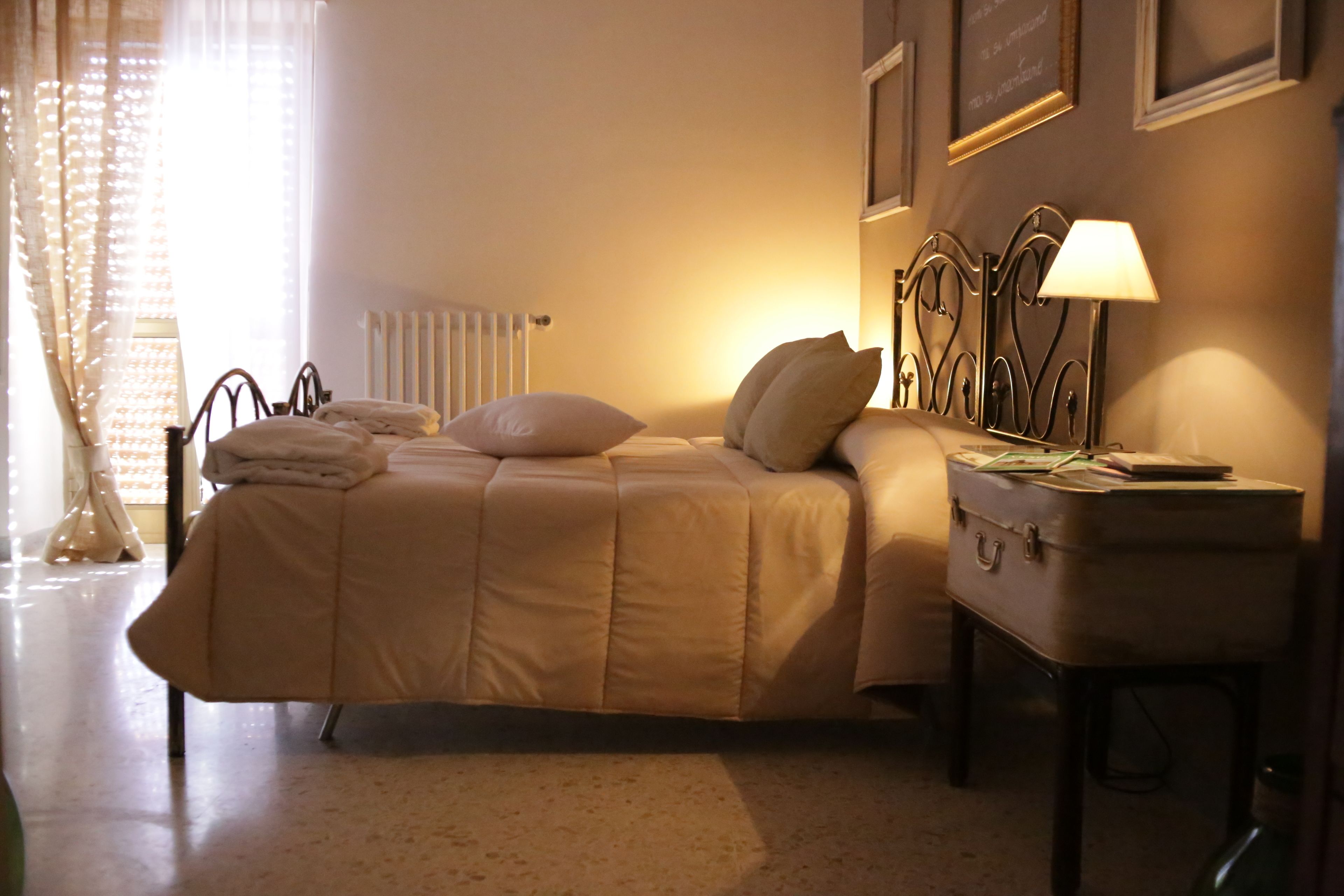Una cama bien tendida con un cabecero, una mesita de noche con una lámpara y un radiador.