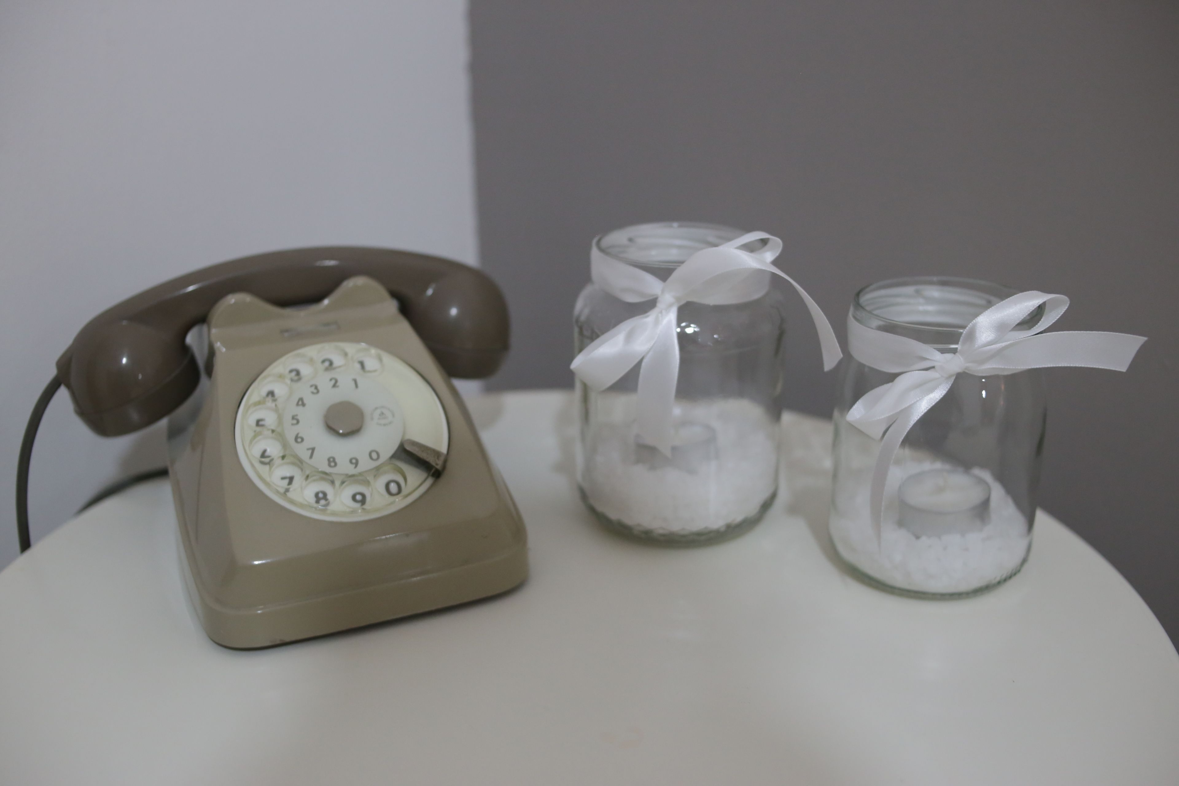 Un telefono a disco d'epoca, due barattoli di vetro con nastri bianchi e una superficie bianca.