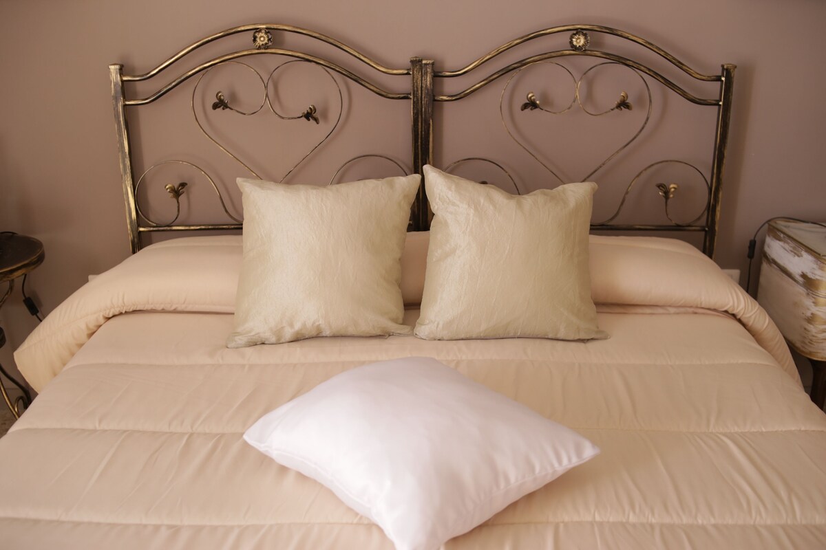 A bed with a metal headboard, two pillows, and a single pillow on a beige bedspread.