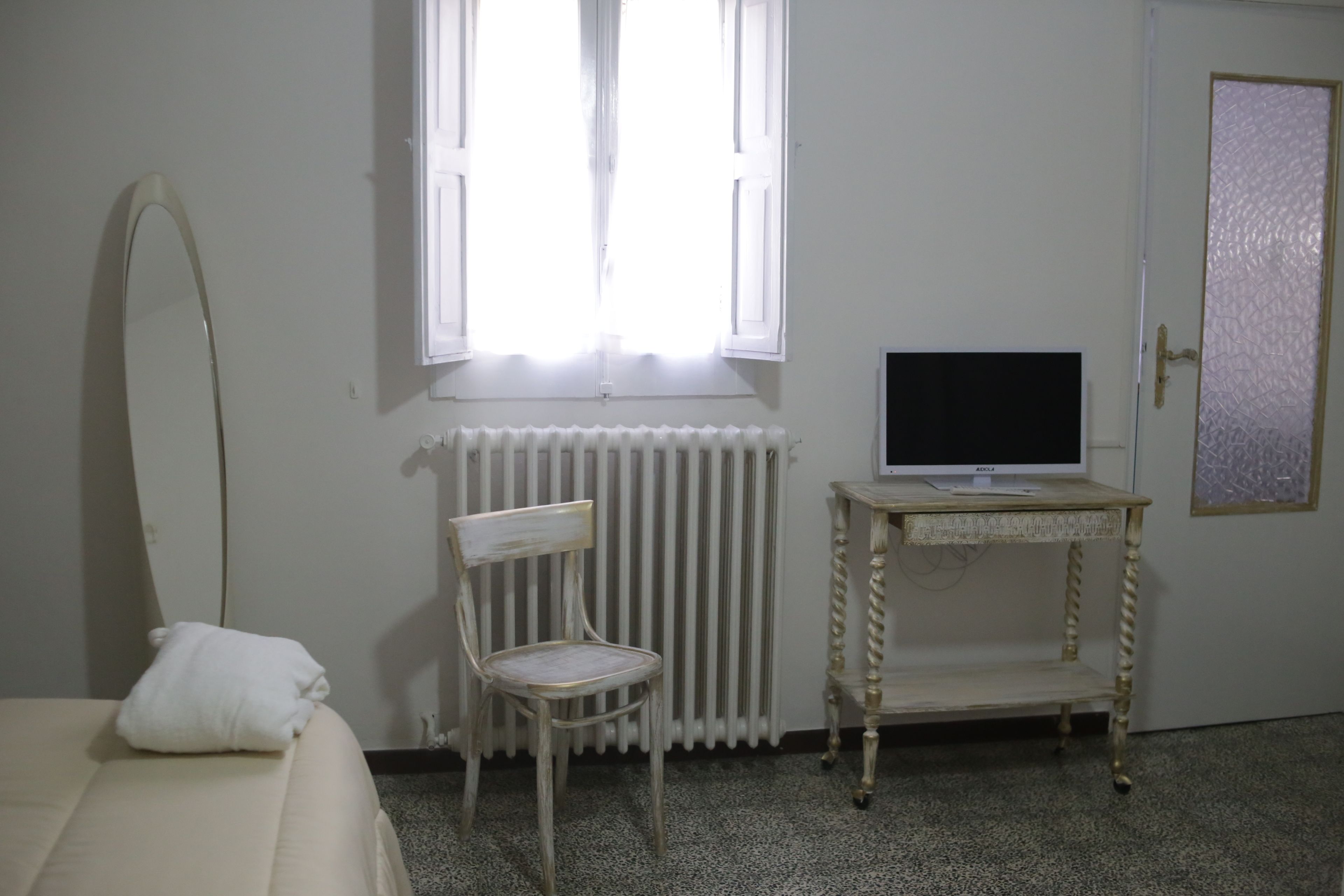 Ein Zimmer mit einem Bett, einem Sessel, einer Heizung, einem Fernseher auf einem kleinen Tisch und einer Tür mit einer Milchglasverglasung.