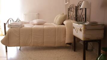 A bed with a beige comforter, a bedside lamp, and a small table with a lamp and books.