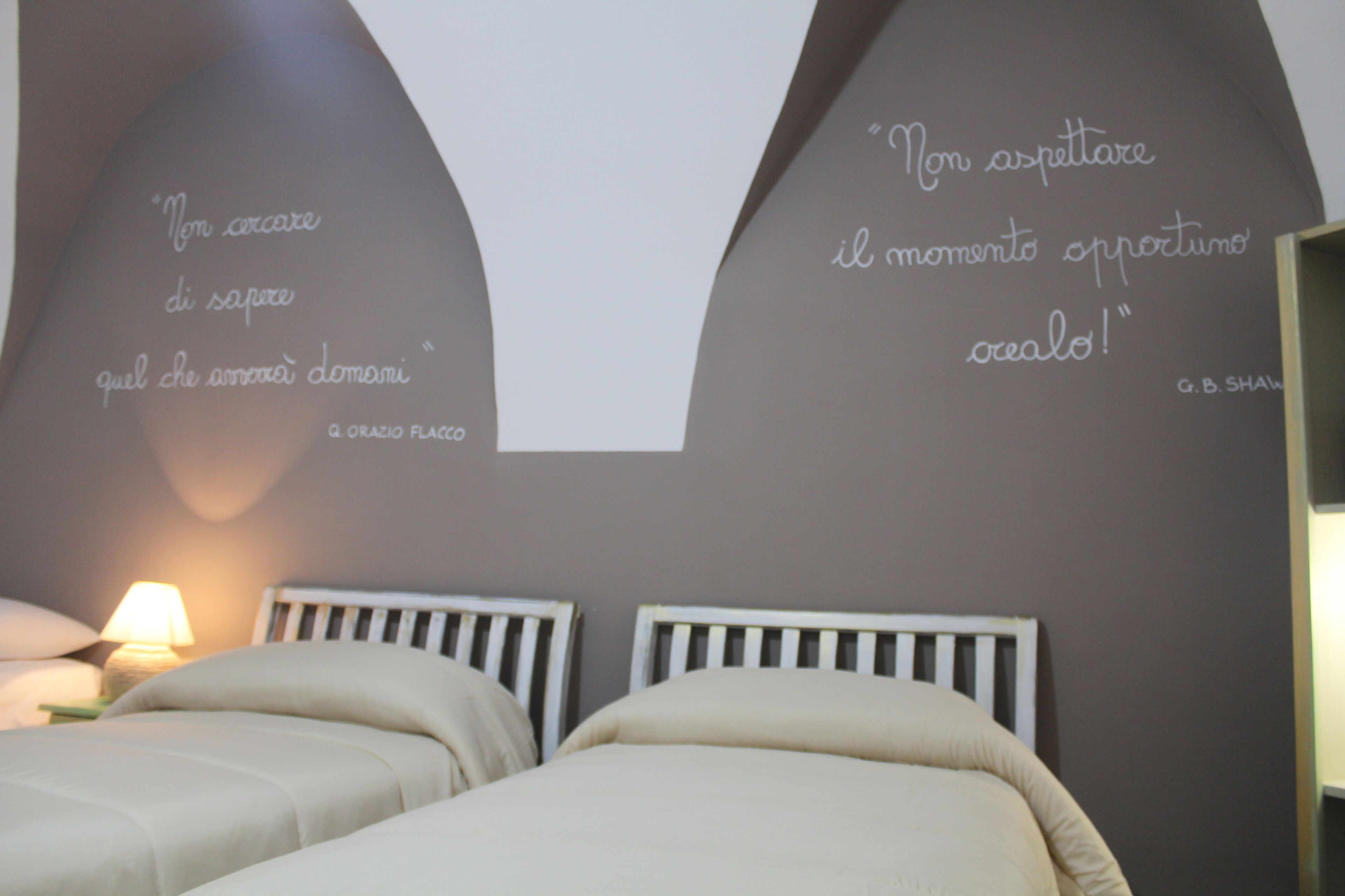 A bedroom with two beds, a wall with inspirational quotes, and a bedside lamp.