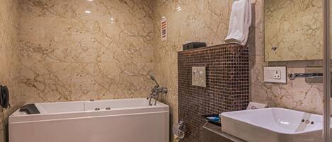 A bathroom with a bathtub, toilet, and sink, marble walls, and a mirror.