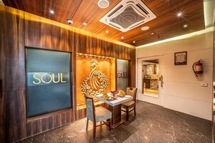 A modern interior with a wooden ceiling, a glass wall with 'SOUL' branding, a decorative wall piece, and a dining area with chairs and a table.