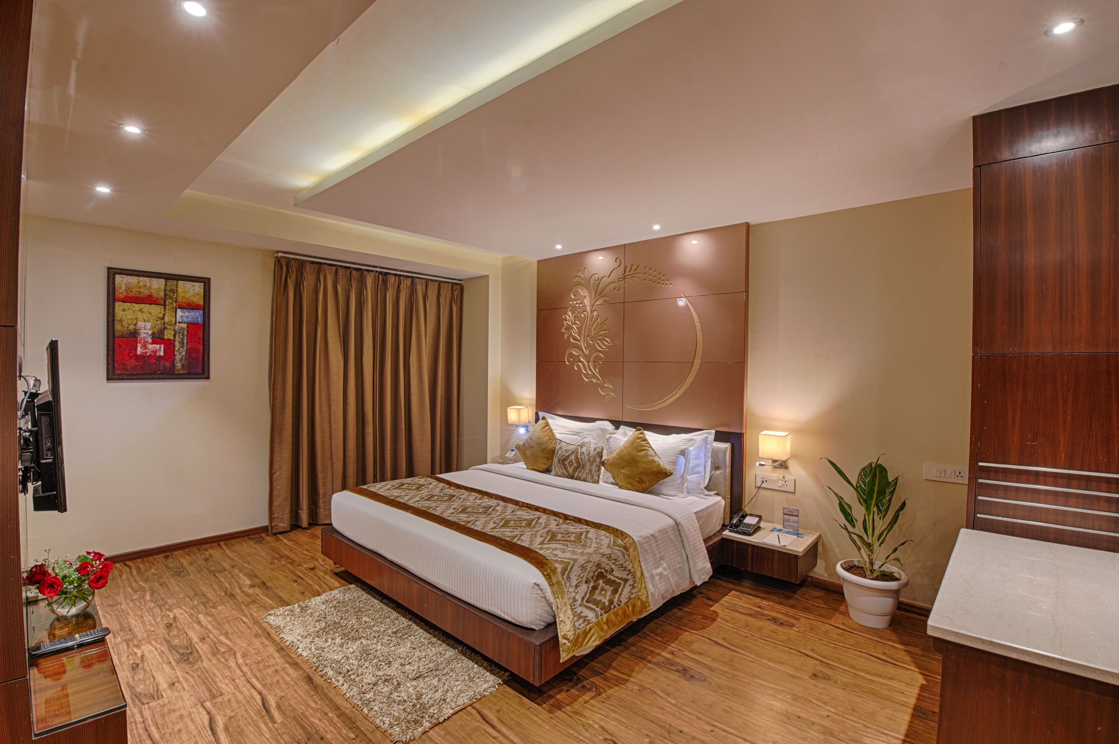A modern hotel room with a large bed, a nightstand, a potted plant, and a wooden floor.