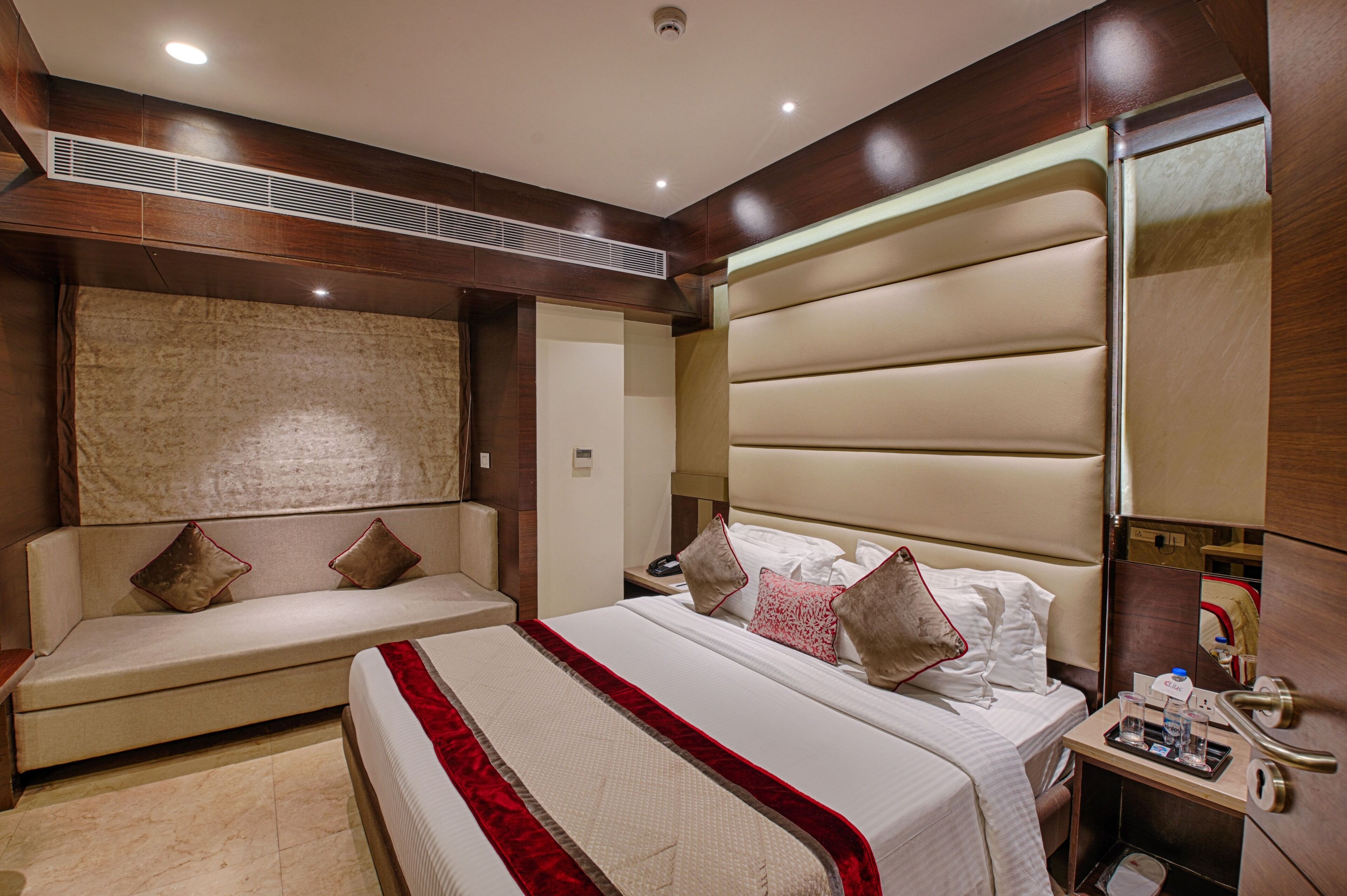 A hotel room with a large bed, a sofa, a bedside table, and a mirror.