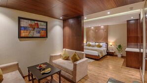 A hotel room with a wooden ceiling, a bed with a nightstand, a sofa with cushions, a small table with a fruit bowl, and a painting on the wall. - Hotel Lilac (Kota)