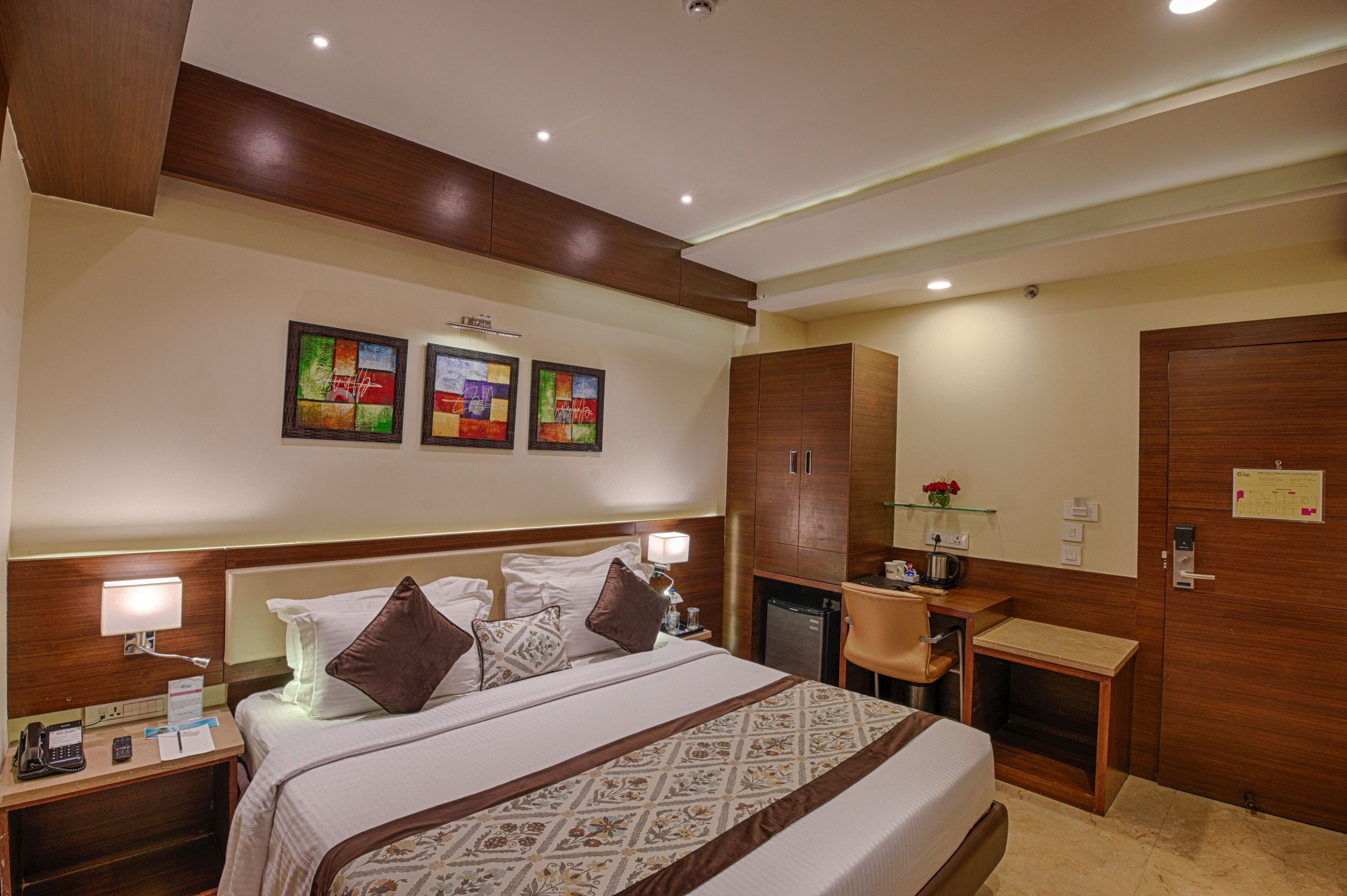 A hotel room with a bed, bedside table, lamp, desk, chair, and wardrobe.