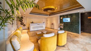 A modern lobby with a reception desk, seating area, and a large screen displaying the hotel name. - Hotel Lilac (Kota)