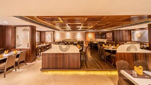 A restaurant with wooden paneling, multiple dining tables, and a central bar area. - Hotel Lilac (Kota)